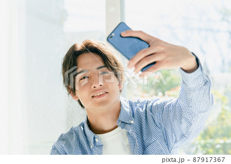 スマホで髪型をチェックする若い男性 スマホで髪型をチェックする若い男性 87917367