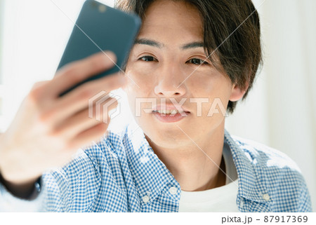 スマホで髪型をチェックする若い男性 スマホで髪型をチェックする若い男性 87917369