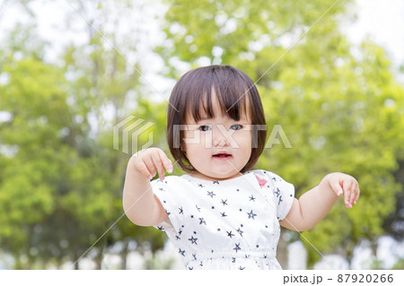 新緑の樹木を背景に笑顔で踊る幼い女の子。育児,教育,躾,愛情,幸せなイメージ 87920266