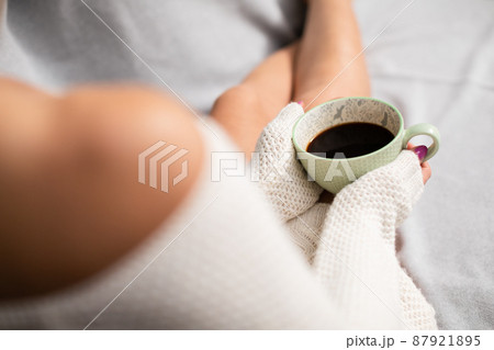 A woman is sitting on a sofa holding a cup of coffee. A woman is sitting on a sofa holding a cup of coffee. 87921895