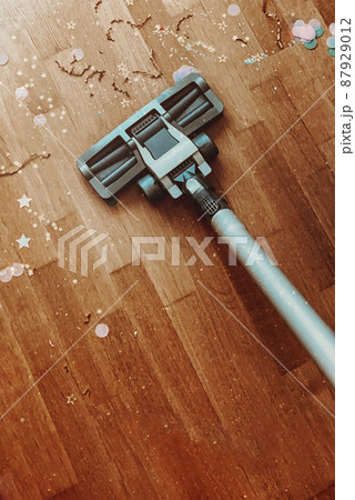 Vacuum cleaner nozzle on wooden floor parquet with confetti, cleaning after Christmas holidays. 87929012