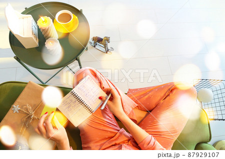 View from above of woman making notes while sitting on sofa with notebook and pen, top view of female wearinng silk pajama planning day or writing todo list during winter holidays. View from above of woman making notes while sitting on sofa with notebook and pen, top view of female wearinng silk pajama planning day or writing todo list during winter holidays. 87929107