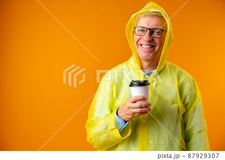 Mature man wearing raincoat over yellow background Mature man wearing raincoat over yellow background 87929307