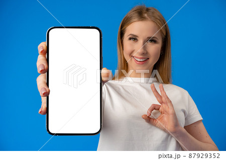 Young smiling woman showing blank screen smartphone in studio 87929352