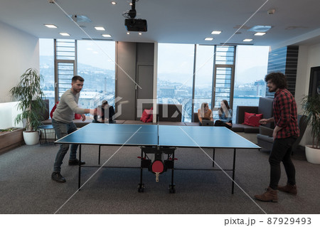 Two young start up business man playing ping pong tennis at modern creative office space people group have meeting and brainstorming in background Two young start up business man playing ping pong tennis at modern creative office space people group have meeting and brainstorming in background 87929493