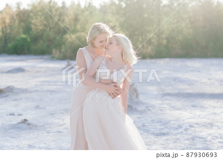 Beautiful lesbian couple walking on sand along river bank on their wedding day 87930693