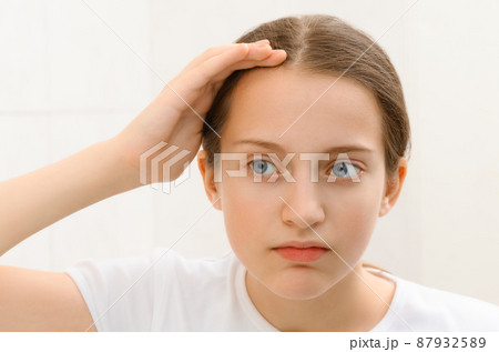 the face of a teenage girl, she looks at herself in the mirror and touches her face with her hand, good and clean skin is a concept of beauty and health the face of a teenage girl, she looks at herself in the mirror and touches her face with her hand, good and clean skin is a concept of beauty and health 87932589