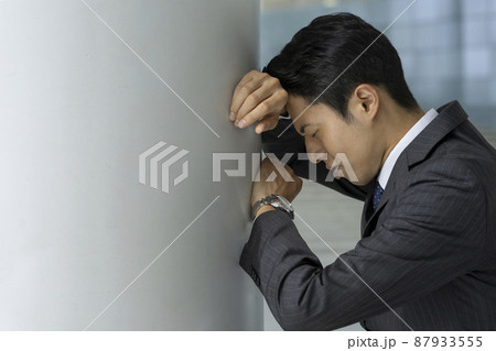 壁にもたれて落ち込む30代のビジネスマンの横顔　悩む・トラブル　イメージ 87933555
