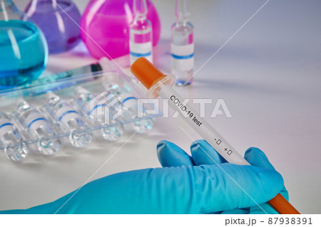 Hand in blue glove holding testing kit. Medical flasks, colorful chemical reagents. Ampoules and syringe isolated on white. Coronavirus. Close up Hand in blue glove holding testing kit. Medical flasks, colorful chemical reagents. Ampoules and syringe isolated on white. Coronavirus. Close up 87938391