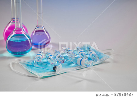 Three medical flasks with purple and pink chemical reagents. Seven mockup ampoules, syringe and mask isolated on white. Coronavirus. Pandemic COVID-19 87938437