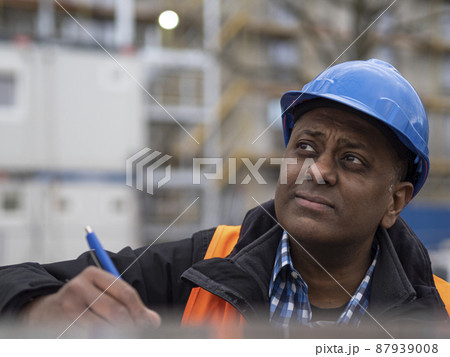 Indian engineer wearing protective workwear checking his projects and signing documents, outdoors Indian engineer wearing protective workwear checking his projects and signing documents, outdoors 87939008