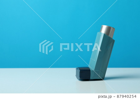 Asthma inhaler on white table against blue background Asthma inhaler on white table against blue background 87940254