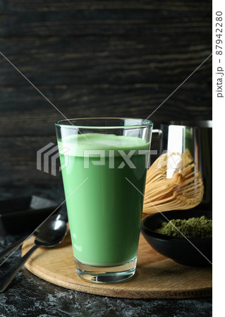 Glass of matcha latte and accessories for making on black smokey table 87942280