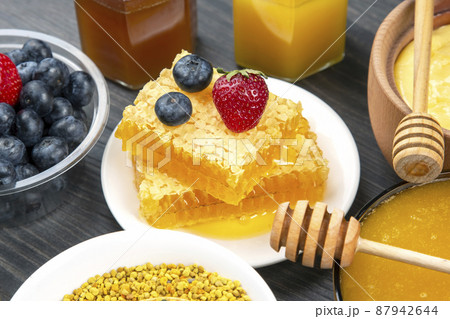 Fresh flower honey of different varieties, pollen and honeycomb with spoons on a wooden background. 87942644