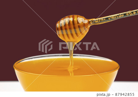 fresh fragrant honey drips from a spoon into a plate on a colored background.  87942855