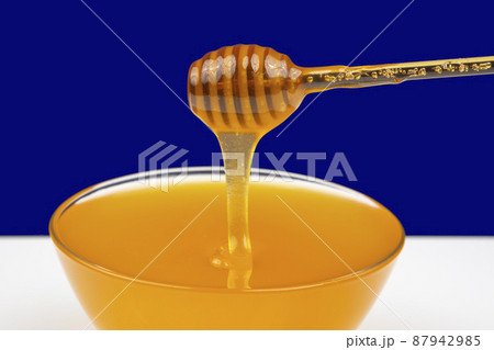 fresh fragrant honey drips from a spoon into a plate on a colored background.  87942985