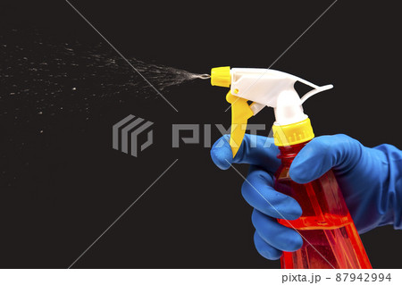 water sprayer bottle in a hand in a protective glove spraying liquid on a dark background. water sprayer bottle in a hand in a protective glove spraying liquid on a dark background. 87942994