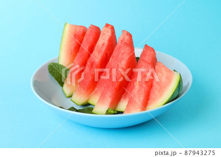 Plate with watermelon slices and mint leaves on blue background Plate with watermelon slices and mint leaves on blue background 87943275
