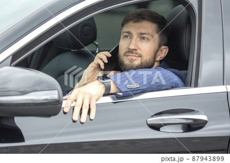 Successful business man with a phone in his hand sits behind the wheel of a prestigious car 87943899