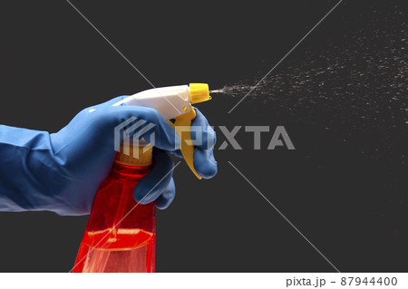 water sprayer bottle in a hand in a protective glove spraying liquid on a dark background water sprayer bottle in a hand in a protective glove spraying liquid on a dark background 87944400