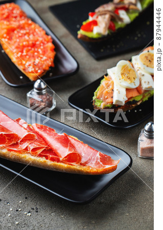 Traditional Spanish breakfast. Tostada with different toppings on a dark background Traditional Spanish breakfast. Tostada with different toppings on a dark background 87944446