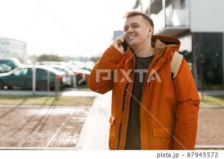 Handsome young man using his phone with smile, guy standing on the street in the city. So glad to hear you. Portrait of excited happy man talking with friend on phone. Urban lifestyle concept. Handsome young man using his phone with smile, guy standing on the street in the city. So glad to hear you. Portrait of excited happy man talking with friend on phone. Urban lifestyle concept. 87945572