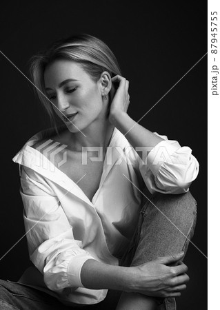 Beautiful blonde woman in a white shirt posing in the studio on a black background. Black and white photo. Model Tests Beautiful blonde woman in a white shirt posing in the studio on a black background. Black and white photo. Model Tests 87945755