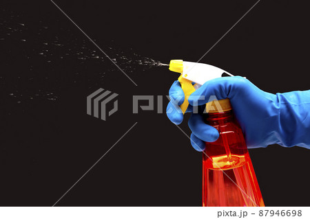 water sprayer bottle in a hand with gloves on a dark background with liquid spray.  87946698
