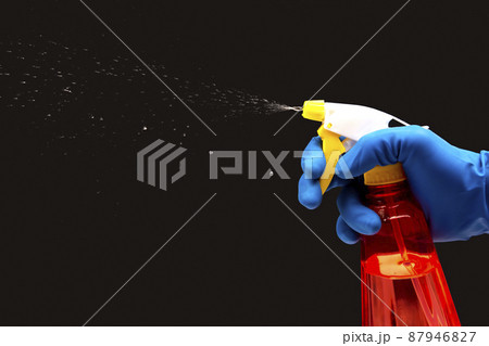 water sprayer bottle in a hand with gloves on a dark background with liquid spray. 87946827