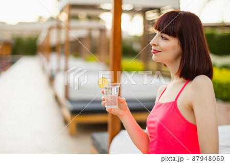 Lifestyle portrait of woman sitting in gazebo near pool and holding fresh drink. Lifestyle portrait of woman sitting in gazebo near pool and holding fresh drink. 87948069