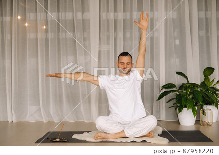 a man in white sportswear is doing yoga with a fitness room. the concept of a healthy lifestyle a man in white sportswear is doing yoga with a fitness room. the concept of a healthy lifestyle 87958220