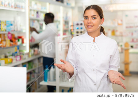 Portrait of a positive young female pharmacist in a pharmacy, standing in the trading floor Portrait of a positive young female pharmacist in a pharmacy, standing in the trading floor 87959978