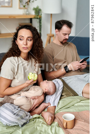 Young serene female with sleeping baby eating fresh green apple Young serene female with sleeping baby eating fresh green apple 87962841