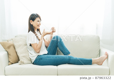 ソファでヨーグルトを食べる女性（笑顔） 87963322