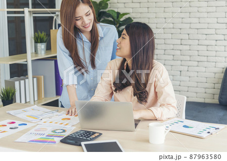 Happiness two women working together confident team meeting in office desk. Team business partners working with computer laptop startup company. Asian colleague friendship at work with smiling face. Happiness two women working together confident team meeting in office desk. Team business partners working with computer laptop startup company. Asian colleague friendship at work with smiling face. 87963580