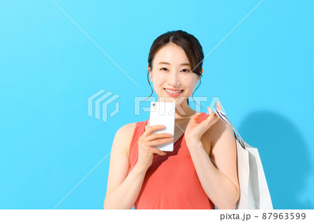 スマホを操作しながら紙袋を持つ若い女性のショッピングイメージ スマホを操作しながら紙袋を持つ若い女性のショッピングイメージ 87963599