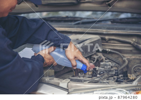 Car Mechanic man hands pouring Deionized purified Distilled water for car battery mechanical service. Close up hands man hold Deionized Distilled liquid water bottle at garage auto mobile car service 87964280
