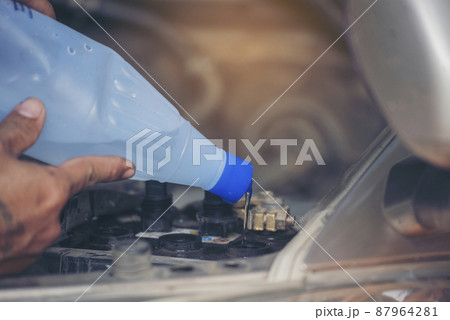 Car Mechanic man hands pouring Deionized purified Distilled water for car battery mechanical service. Close up hands man hold Deionized Distilled liquid water bottle at garage auto mobile car service Car Mechanic man hands pouring Deionized purified Distilled water for car battery mechanical service. Close up hands man hold Deionized Distilled liquid water bottle at garage auto mobile car service 87964281