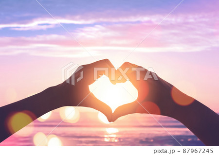 Female hands heart shape on sunset sky at tropical beach abstract background. Female hands heart shape on sunset sky at tropical beach abstract background. 87967245