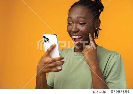 Happy smiling african american girl using her smartphone in yellow studio. Happy smiling african american girl using her smartphone in yellow studio. 87967391
