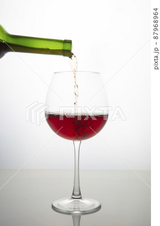 red wine from a bottle is poured into a glass on a light background 87968964