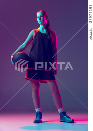 Portrait of teenager basketball player in uniform posing isolated over gradient pink purple background in neo 87972195