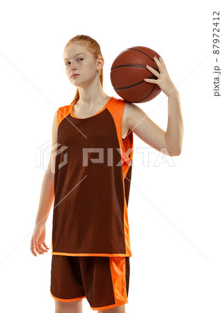 Portrait of red haired girl, teenager, basketball player in uniform posing with ball on shoulder isolated over white studio background Portrait of red haired girl, teenager, basketball player in uniform posing with ball on shoulder isolated over white studio background 87972412