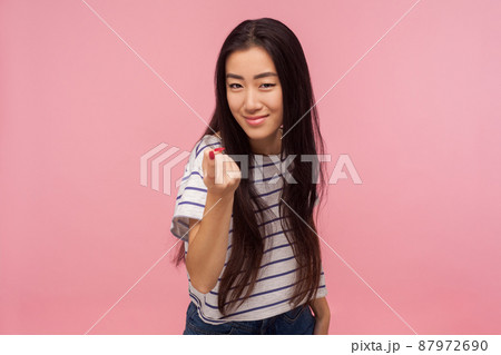 Come here, Portrait of attractive girl with brunette hair in striped t-shirt gesturing come to me, beckoning with finger, inviting for confidential talk. indoor studio shot isolated on pink background Come here, Portrait of attractive girl with brunette hair in striped t-shirt gesturing come to me, beckoning with finger, inviting for confidential talk. indoor studio shot isolated on pink background 87972690