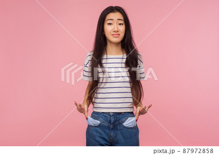 Unemployment and bankruptcy. Upset poor girl with brunette hair in striped t-shirt turning out empty pockets, worried about debts, no cash for living. indoor studio shot isolated on pink background 87972858