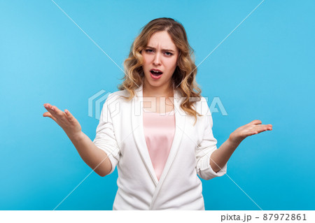 How could you, Portrait of disgruntled woman with wavy hair in white jacket indignantly asking reason of failure, claims in conflict, why hand gesture. indoor studio shot isolated on blue background 87972861