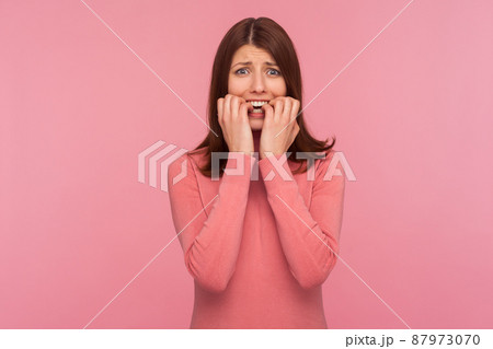 Nervous confused brunette woman in pink sweater biting nails on her fingers in panic, depression, sadness. Indoor studio shot isolated on pink background Nervous confused brunette woman in pink sweater biting nails on her fingers in panic, depression, sadness. Indoor studio shot isolated on pink background 87973070