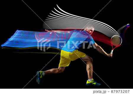 One man, professional tennis player playing tennis isolated on dark background with mixed colored stipes. Concept of sport, hobby, challenges, peace, politics 87973207