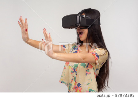 Amazed happy woman in VR glasses standing with raised palms, playing video game saying wow, experiencing excited emotions while using virtual reality 3d headset. indoor studio shot, pink background 87973295