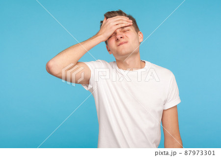 Oh no, I forgot. Portrait of unlucky man in casual white t-shirt making facepalm gesture, feeling regret and shame about forgotten event, bad memory. indoor studio shot isolated on blue background Oh no, I forgot. Portrait of unlucky man in casual white t-shirt making facepalm gesture, feeling regret and shame about forgotten event, bad memory. indoor studio shot isolated on blue background 87973301